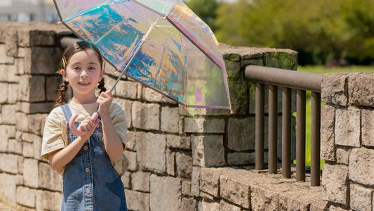Young girl holding a colourful reflective umbrella outdoors near a stone wall.