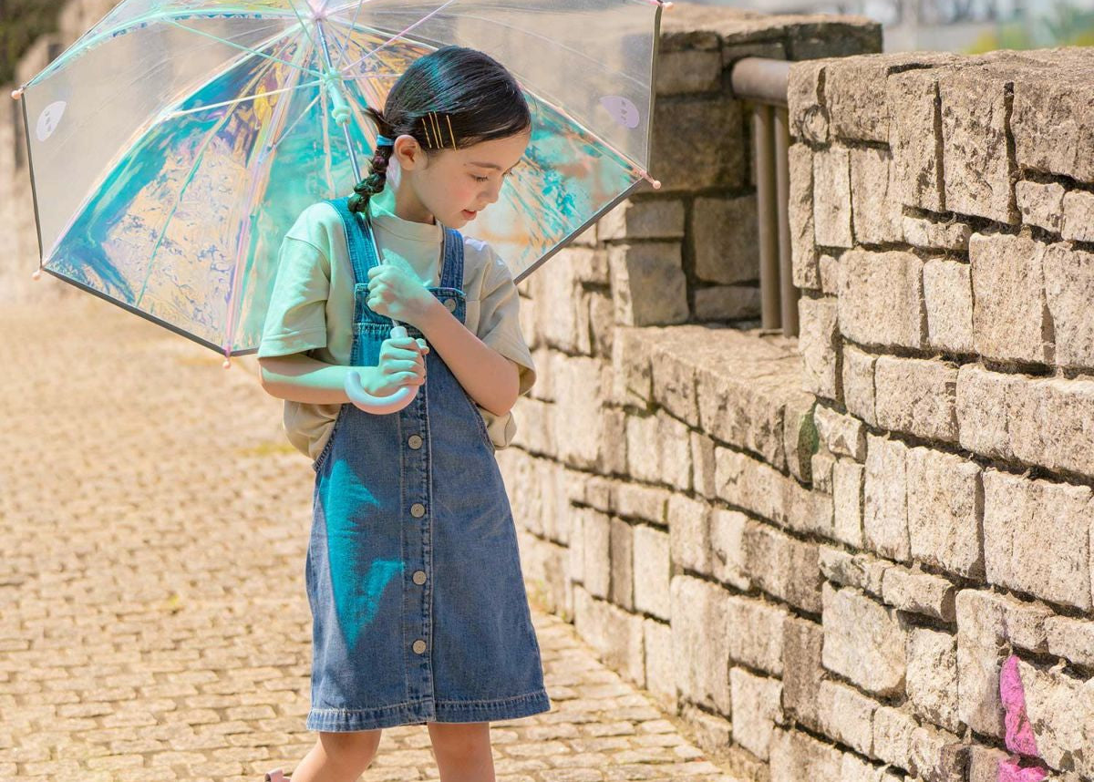 Child holding a light shiny reflective umbrella with a stone wall and pavement background. Designed in Japan