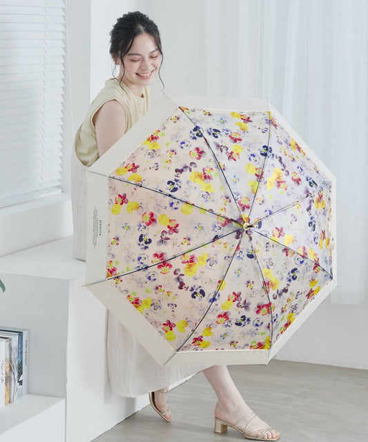 Smiling woman holding the limited edition Wpc x Plantica Joyful Floral translucent vinyl umbrella in the Multi-color pattern