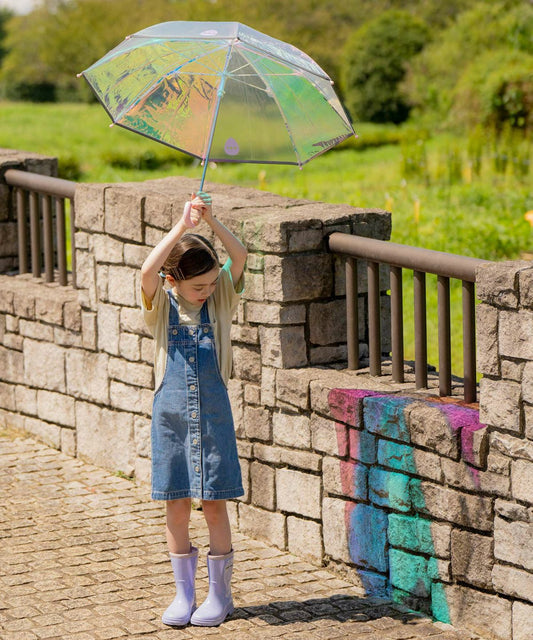 Child holding a transparent umbrella with a colourful reflective shine, standing on a stone pathway.